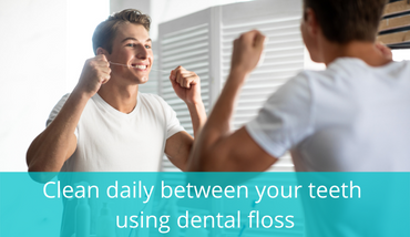young man cleaning between his teeth with dental floss looking at the mirrow